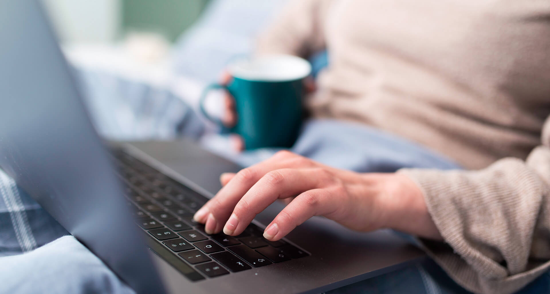 Frau mit Laptop und Kaffeetasse gemütlich auf der Couch