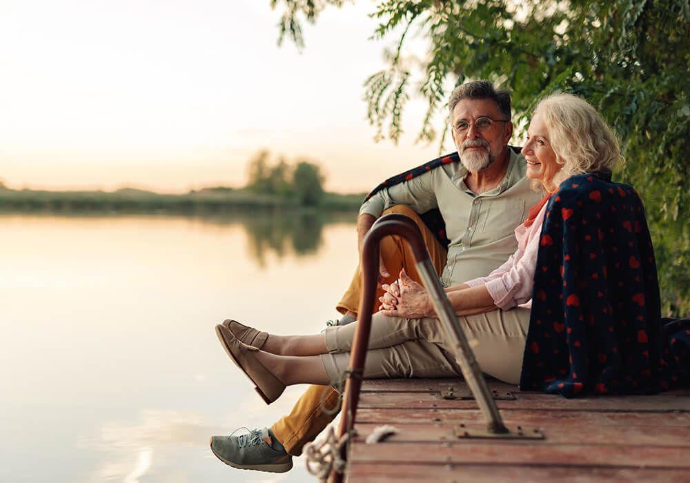 Älteres Paar hält sich an den Händen und genießt einen ruhigen Sonnenuntergang am See 