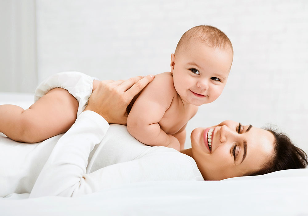 Junge Mutter hält lächelnd ihr Baby in die Luft